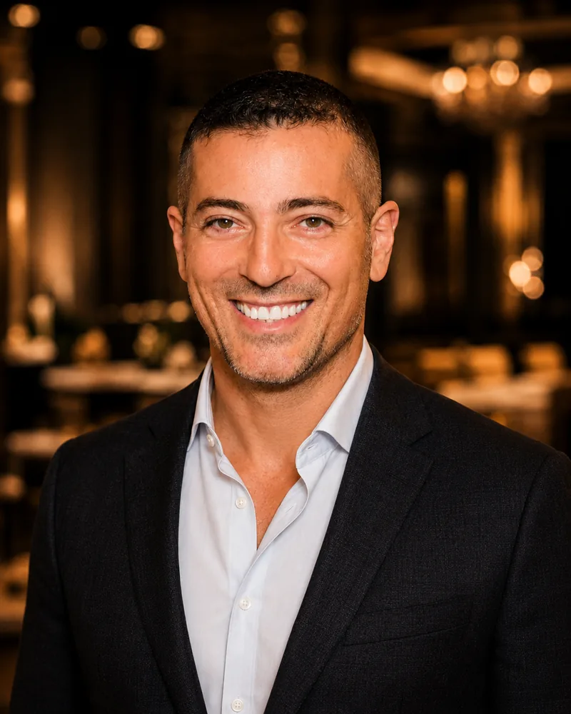 Shane Black smiling in a dark blazer and open-neck shirt at a luxury event venue